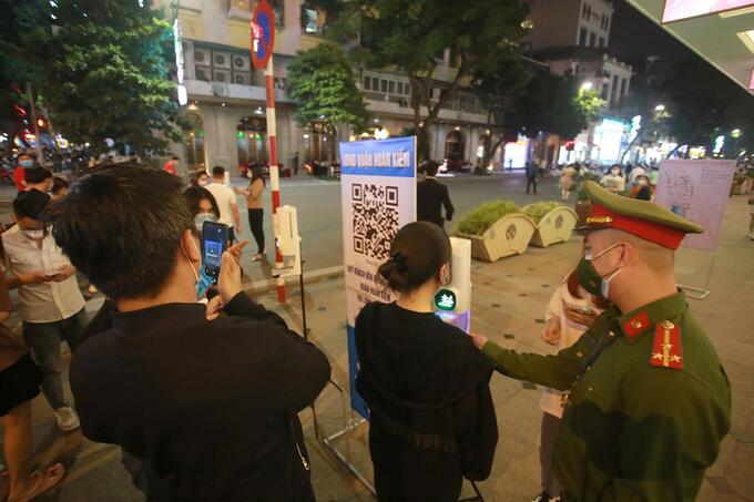 Người dân quét mã QR khai báo y tế, sát khuẩn tay và đo thân nhiệt trước khi vào phố đi bộ. Ảnh ANTĐ