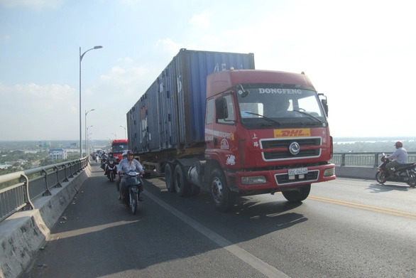 Một chiếc xe đầu kéo kéo theo container ì ạch “bò” lên cầu Rạch Miễu, phía sau là dòng xe đang nhẫn nại “bò” theo | Ảnh: MẬU TRƯỜNG
