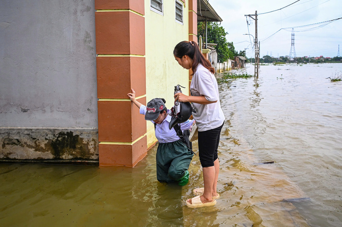 Một phụ huynh khác đưa con ra đầu ngõ để đi học. Nhìn con lên tới điểm cao, không ngập, chị này mới yên tâm ra về
